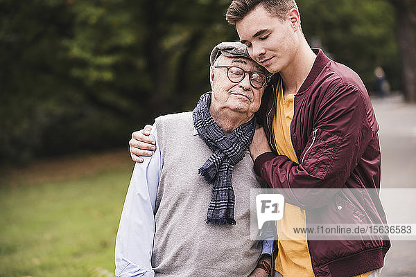 Portrait of senior man head to head with his adult grandson outdoors