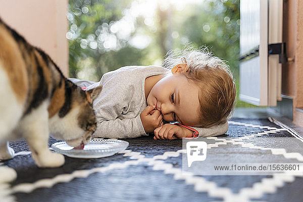 Süßes Kleinkind-Mädchen beobachtet Katze beim Trinken aus dem Napf