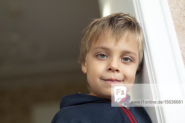 Porträt eines kleinen Jungen  der sich gegen eine Türkiste lehnt