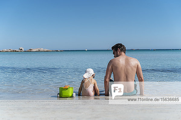 Rückansicht eines im Meer sitzenden Vaters mit Tochter