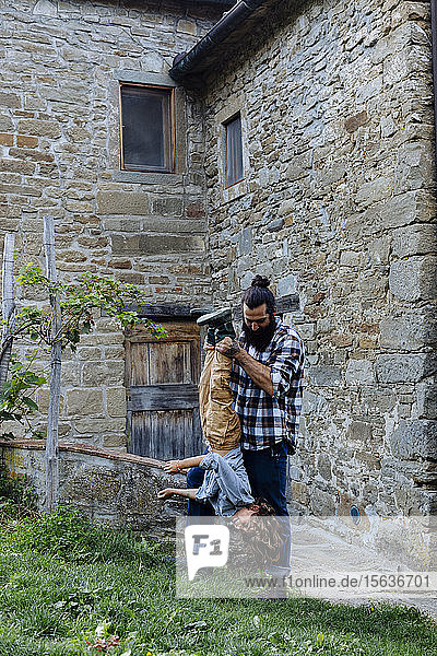 Father holding son upside down at a rustic farmhouse