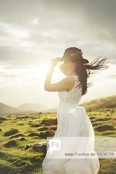 Junge Frau in weißem Kleid auf Aussichtspunkt bei Sonnenuntergang