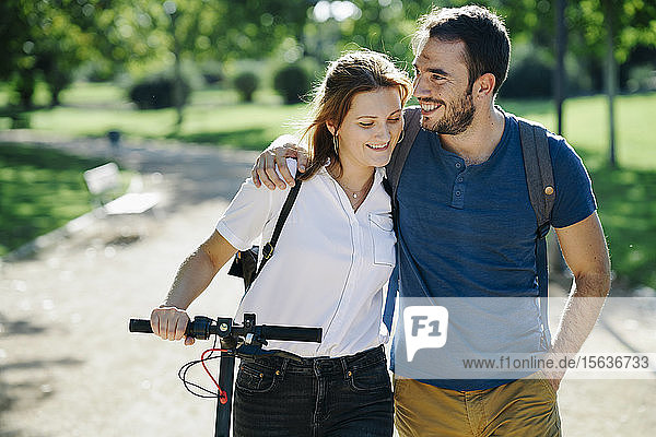 Glückliches Paar mit Elektroroller in einem Stadtpark