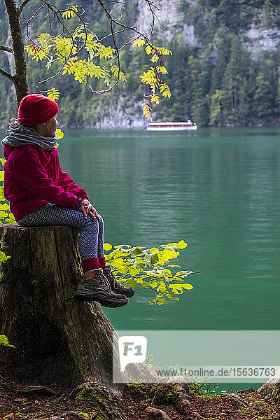 Deutschland  Oberbayern  Mädchen auf Baumstumpf am Keonigssee sitzend