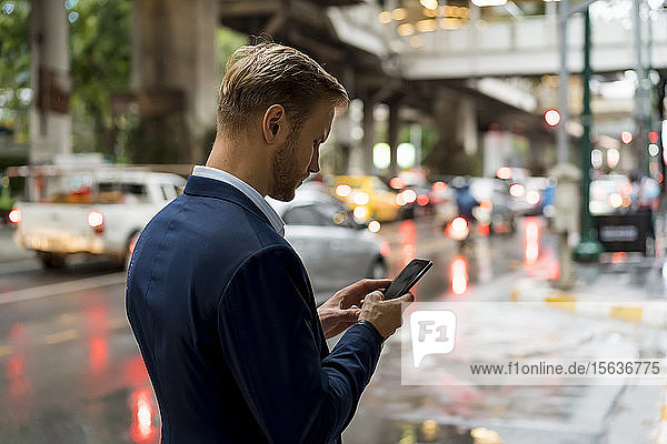 Young businessman using smartphone in Bangkok during a rainy day