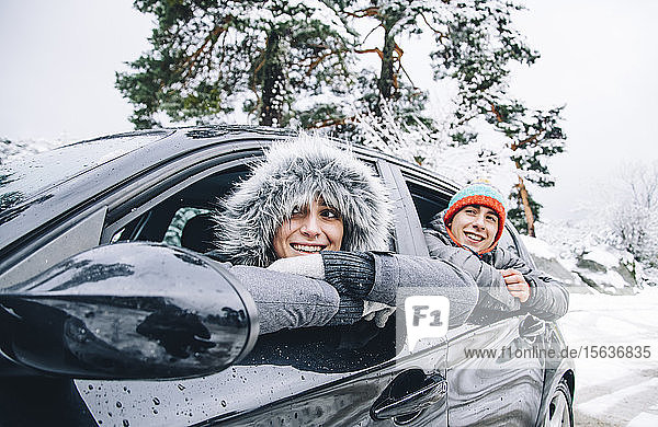 Porträt eines glücklichen jungen Paares  das in einem Auto im Winterwald sitzt und Spaß hat
