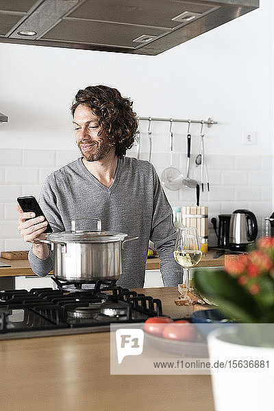 Smiling man using cell phone in kitchen at home