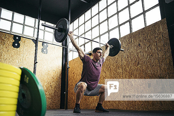 Young man doing overhead squat exercise at gym