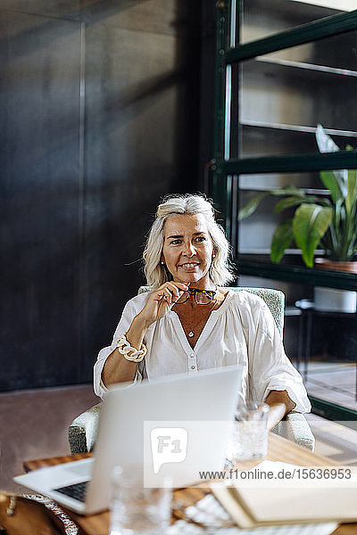 Porträt einer lächelnden reifen Geschäftsfrau mit Laptop im Loft-Büro