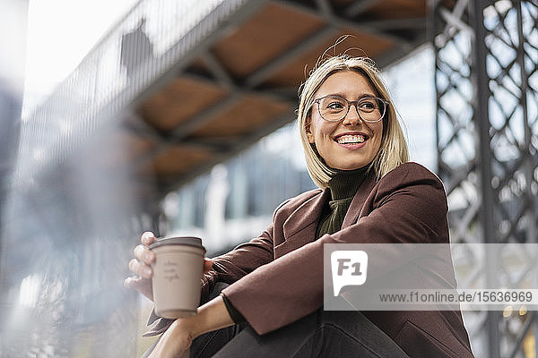 Fröhliche junge Geschäftsfrau mit Kaffee zum Mitnehmen in der Stadt