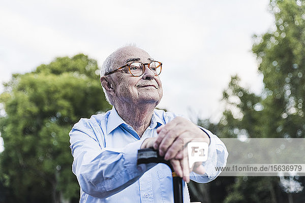 Portrait of senior man in a park leaning on his walking stick