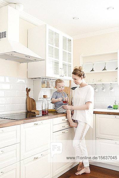Mutter mit ihrem kleinen Jungen  der in der Küche einen Saft trinkt