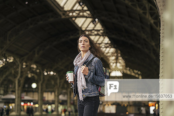 Junge weibliche Reisende mit Kaffee zum Mitnehmen auf den Bahnsteig