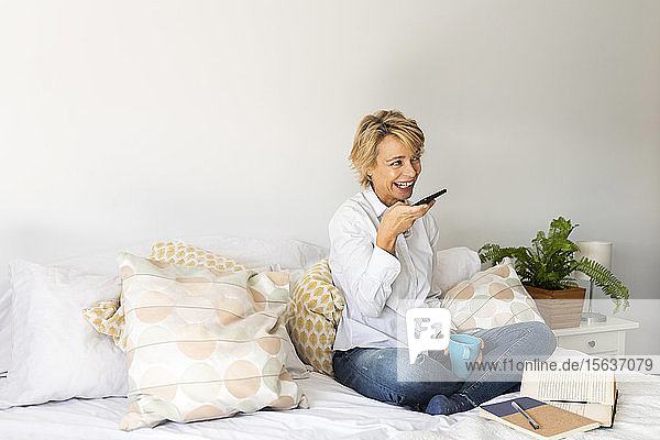 Reife Frau sitzt zu Hause im Bett und benutzt ein Smartphone