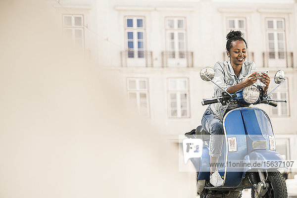 Lächelnde junge Frau mit Motorroller und Mobiltelefon in der Stadt  Lissabon  Portugal
