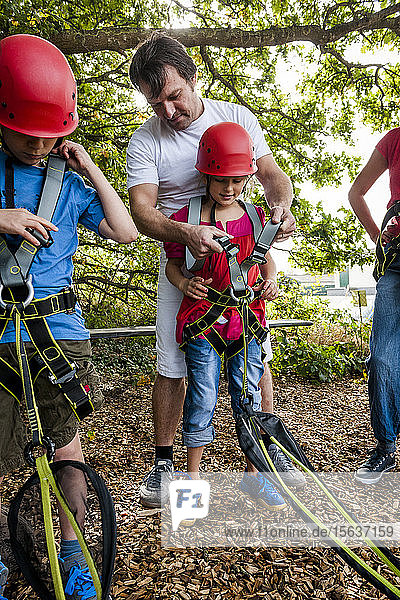 Man helping girl preparing for a rope course in forest
