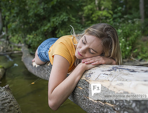 Frau liegt auf einem Baumstamm am Seeufer
