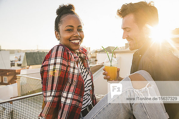 Glückliches junges Paar trinkt bei Sonnenuntergang auf dem Dach