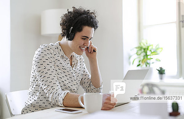 Lächelnde junge Frau mit Headset und Laptop bei der Arbeit am Schreibtisch