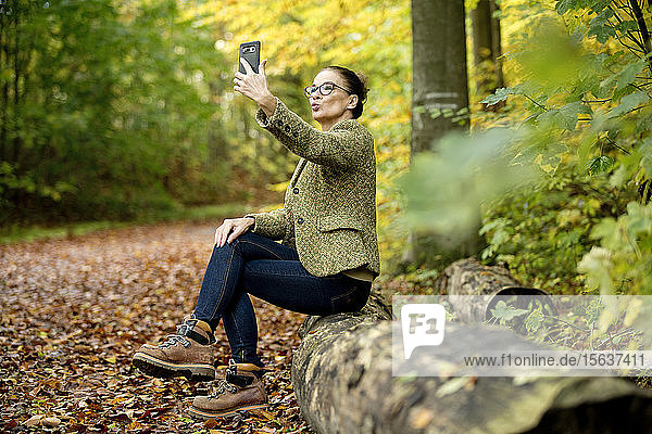 Eine reife Frau  die in einem Herbstwald ein Selfie macht
