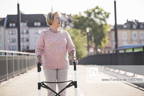 Ältere Frau mit Gehhilfe auf Rädern auf Fußgängerbrücke