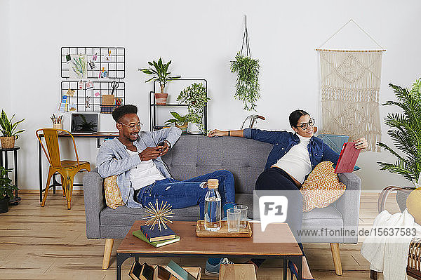 Multiethnisches Paar verbringt Zeit zusammen im Wohnzimmer  Frau mit Tablet und Mann mit Smartphone