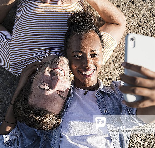 Glückliches junges Paar liegt auf dem Betonboden und macht sich ein Selfie
