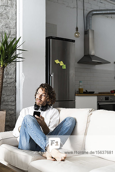 Relaxed man sitting on couch at home with cell phone
