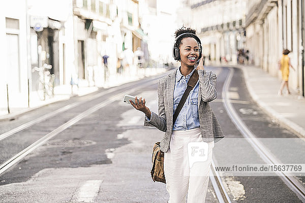 Happy young woman with headphones and mobile phone in the city on the go  Lisbon  Portugal