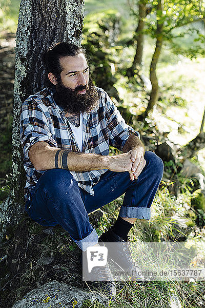 Mann mit Bart sitzt am Baumstamm im Wald