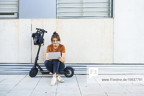 Porträt einer Frau  die auf einem Elektroroller sitzt und ein digitales Tablet benutzt