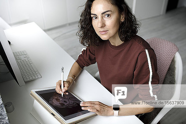 Weibliche Webdesignerin  die zu Hause ein Tablet benutzt und in die Kamera schaut