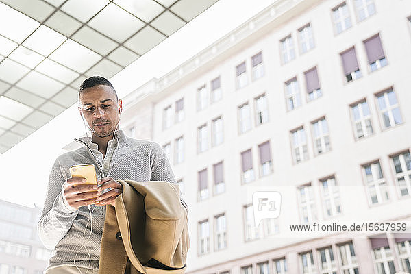 Porträt eines Geschäftsmannes mit Kopfhörern mit Smartphone in der Stadt