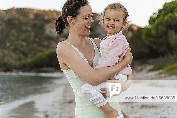 Glückliche Mutter trägt ihre Tochter am Strand