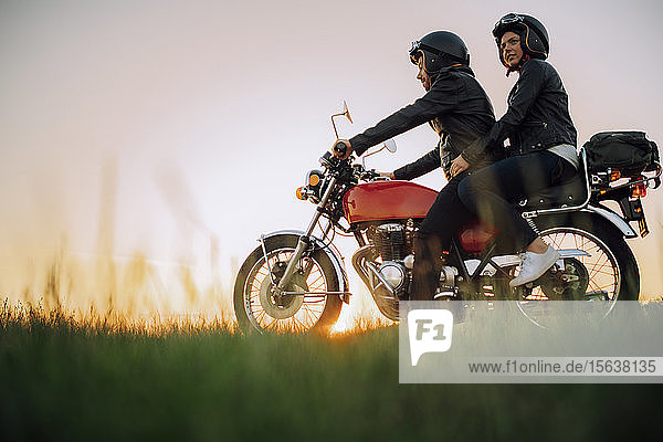 Junges Paar auf einem Oldtimer-Motorrad bei Sonnenuntergang