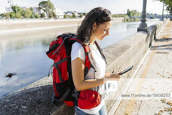 Junge Rucksacktouristin mit Smartphone an einem Fluss in Verona  Italien