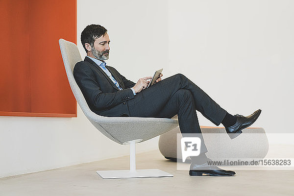 Reifer Geschäftsmann auf Stuhl sitzend mit Tablett