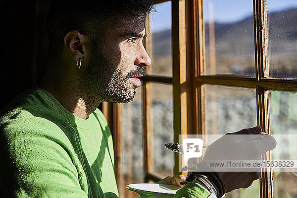 Mann isst Müsli zum Frühstück  während er durch das Fenster schaut