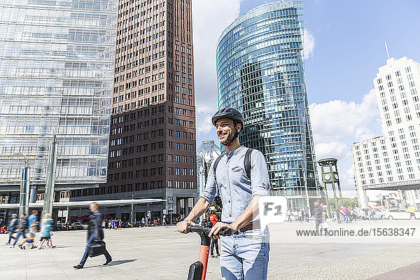 Businessman with e-scooter on city square  Berlin  Germany