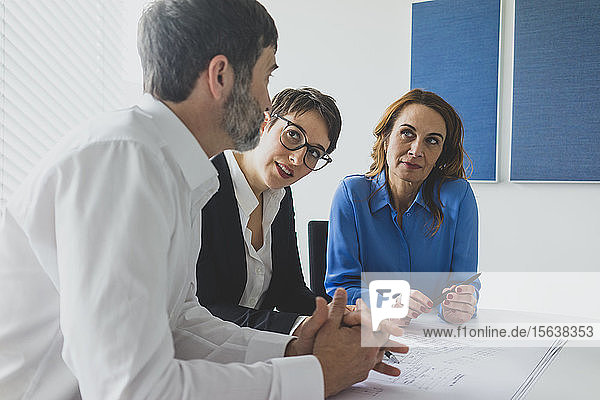 Geschäftsmann und zwei Geschäftsfrauen arbeiten an einem Plan auf dem Schreibtisch im Büro
