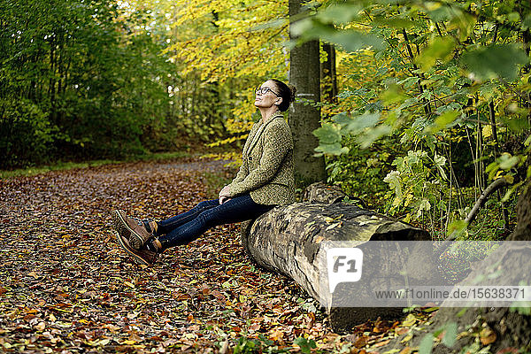 Reife Frau sitzt auf einem Baumstamm in einem Herbstwald