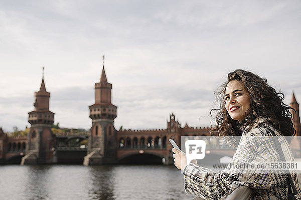 Lächelnde Frau mit Smartphone in der Stadt an der Oberbaumbrücke  Berlin  Deutschland