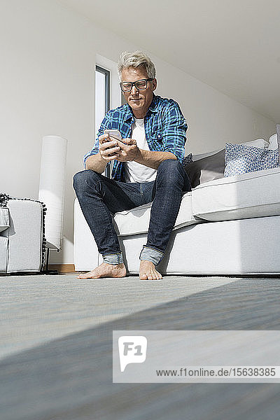 Lässiger Geschäftsmann  der in einem modernen Haus sitzt und ein Smartphone benutzt