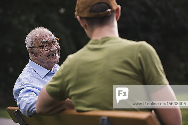 Porträt eines lächelnden älteren Mannes  der sich zusammen mit seinem Enkel auf einer Parkbank entspannt