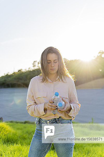 Porträt einer jungen Frau im Gegenlicht  die zwei leere Plastikflaschen hält