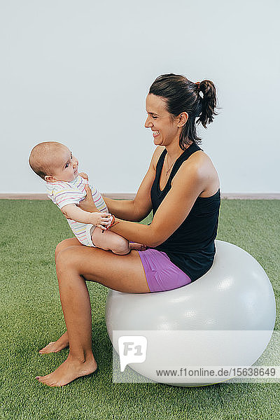 Junge Mutter und Baby trainieren auf dem Fitnessball