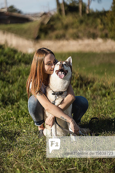 Glückliche junge Frau umarmt ihren Hund auf einer Wiese