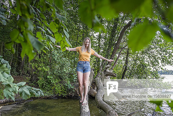 Lächelnde Frau balanciert auf einem Baumstamm am Seeufer
