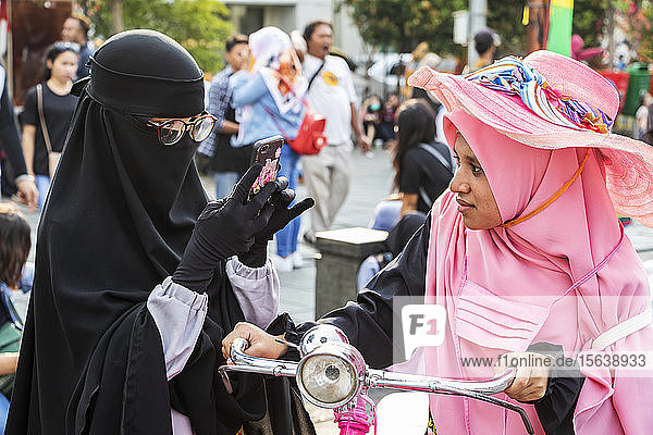 Frauen auf dem Taman Fatillah-Platz  eine mit einem Smartphone  die andere auf einem Fahrrad; Jakarta  Java  Indonesien