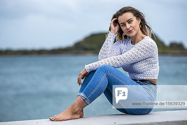 Portrait of a young woman sitting on a wall along the ocean; Wellington  North Island  New Zealand